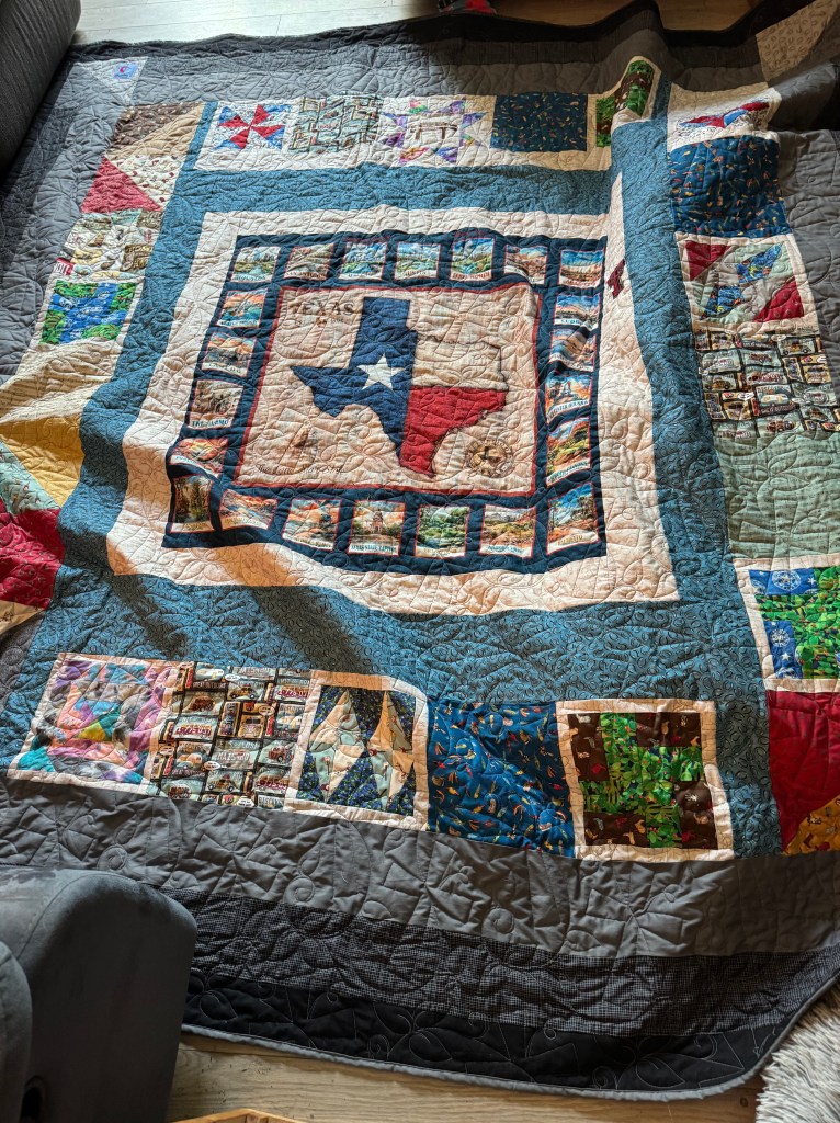 An intricately designed quilt featuring a central Texas state motif surrounded by colorful patchwork pieces, laid out on a wooden floor.