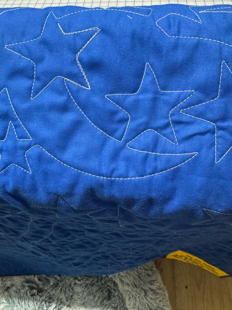 Close-up of a blue quilt featuring white stitched stars and a crescent moon pattern.