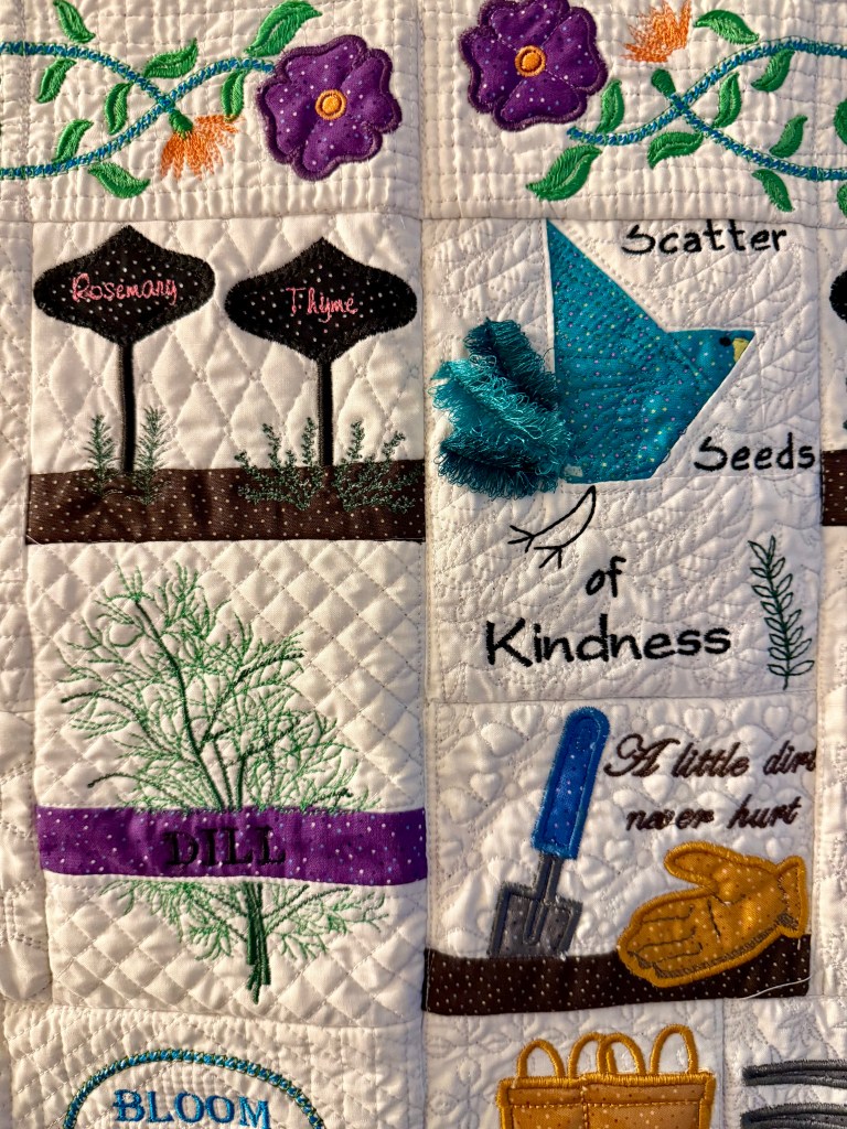 A colorful quilt featuring embroidered herbs like rosemary, thyme, and dill, along with a blue bird and phrases about kindness and gardening.